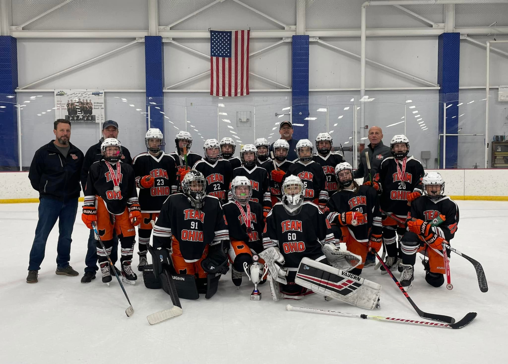 Team Ohio youth hockey team posed on the ice with coaches and a trophy