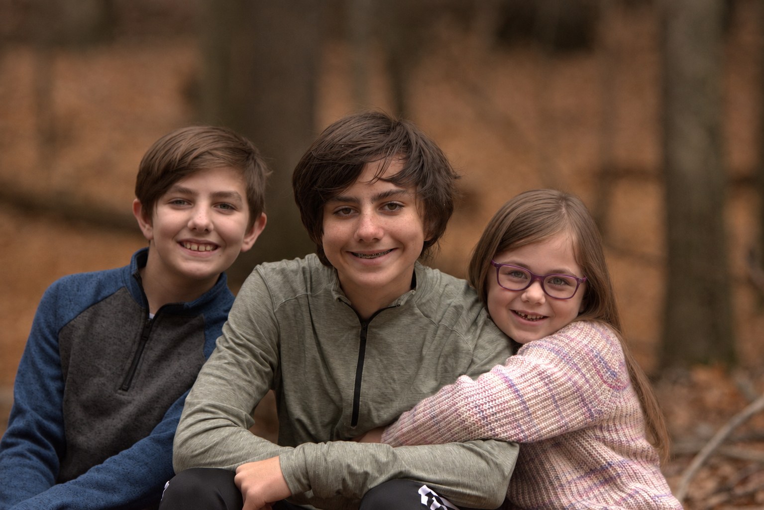 Three smiling siblings photographed together in an autumn woodland